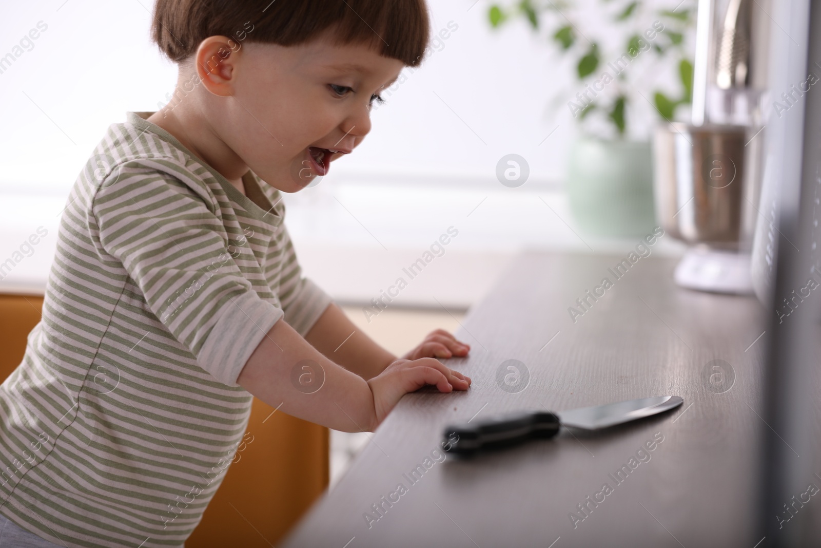 Photo of Little boy reaching towards knife on kitchen counter. Dangerous situation