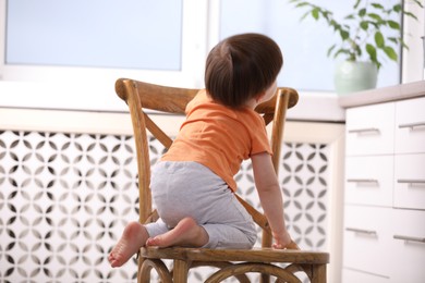 Photo of Little boy playing on chair in kitchen. Dangerous situation