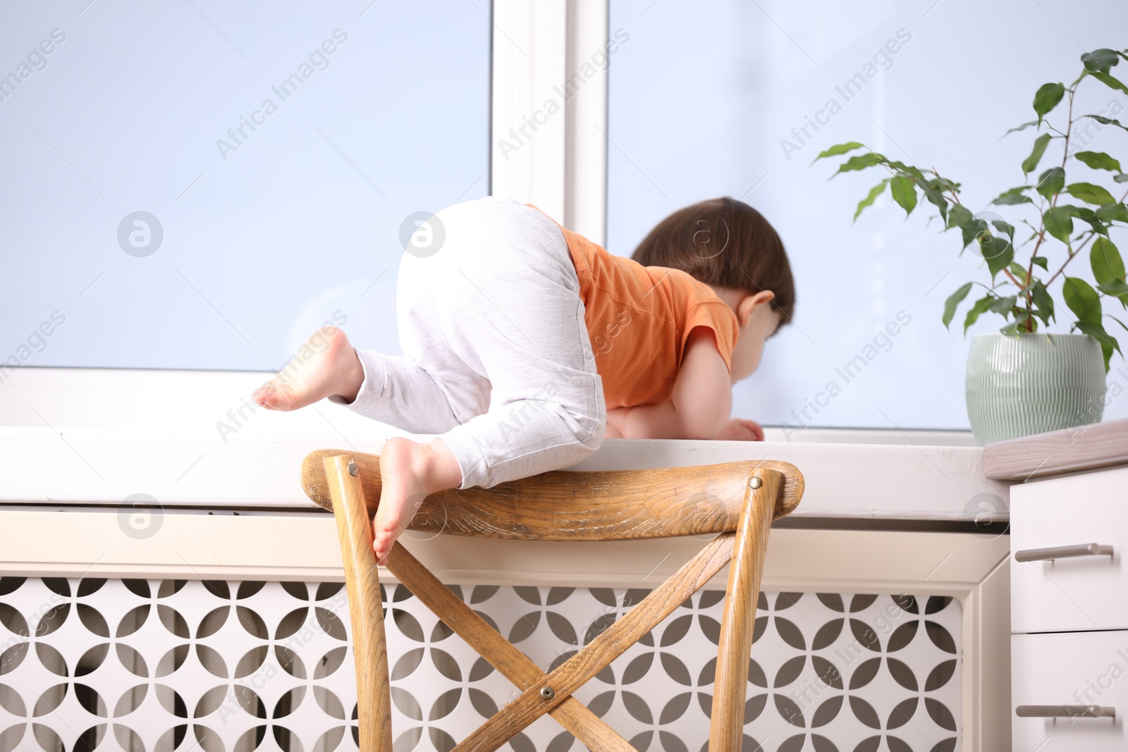 Photo of Little boy near window on windowsill, back view. Dangerous situation