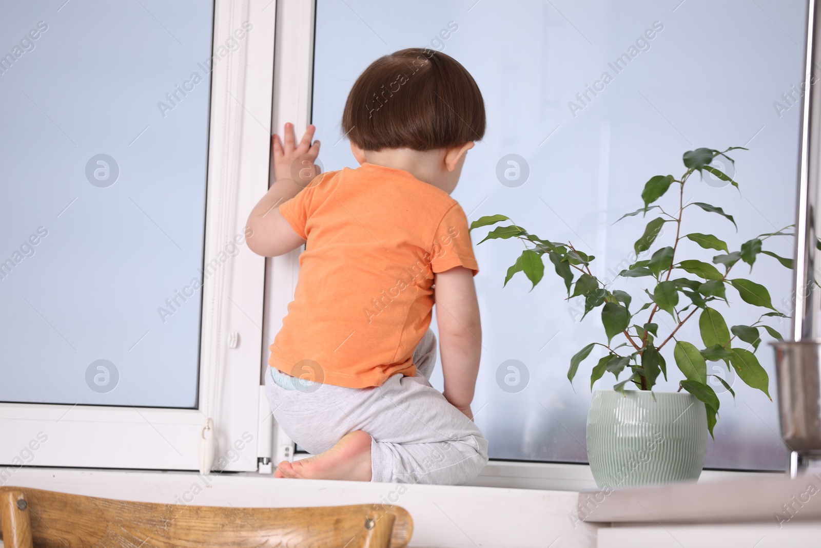 Photo of Little boy near window on windowsill, back view. Dangerous situation