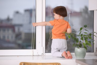 Photo of Little boy near window on windowsill, back view. Dangerous situation