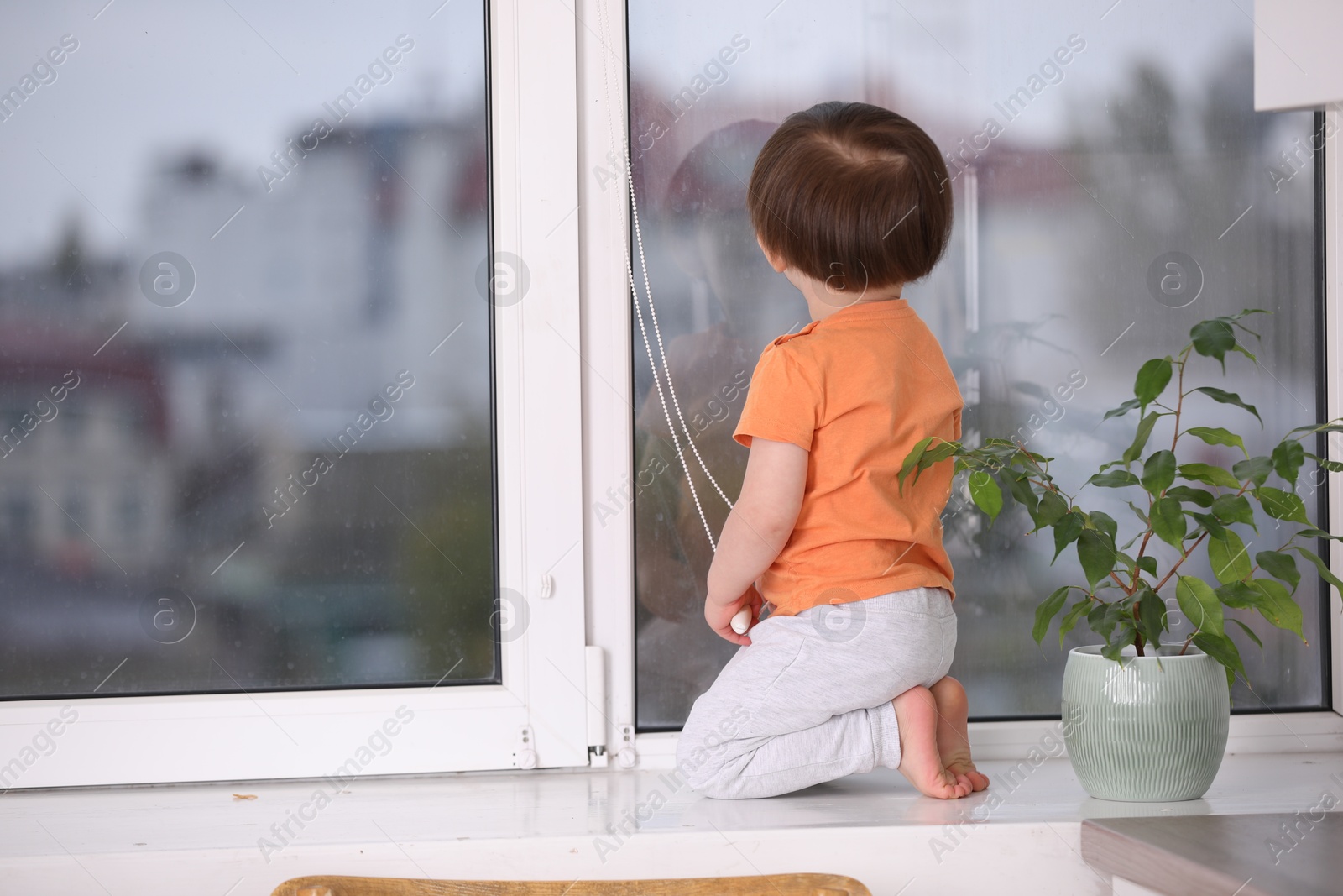 Photo of Little boy near window on windowsill, back view. Dangerous situation