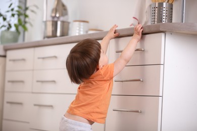 Photo of Little boy playing with kitchen appliances indoors, back view. Dangerous situation