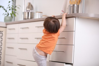 Photo of Little boy playing with kitchen appliances indoors, back view. Dangerous situation