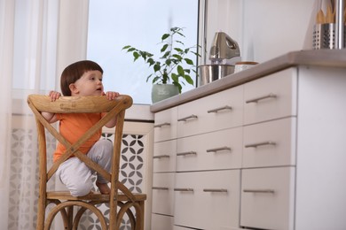 Photo of Little boy playing on chair in kitchen. Dangerous situation