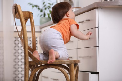 Photo of Little boy playing on chair in kitchen. Dangerous situation