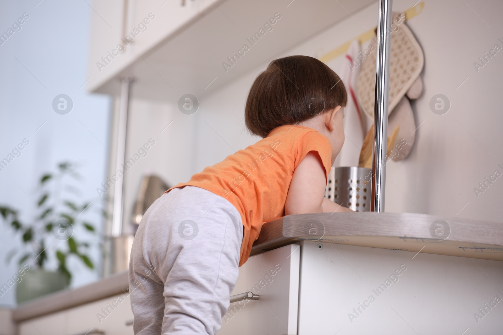 Photo of Little boy playing with kitchen appliances indoors, back view. Dangerous situation