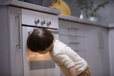 Photo of Little boy playing with oven in kitchen. Dangerous situation