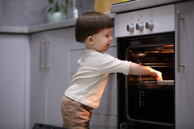 Photo of Little boy playing with oven in kitchen. Dangerous situation