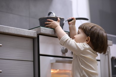 Photo of Little boy playing with pot on stove in kitchen. Dangerous situation