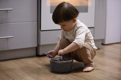 Photo of Little boy playing with pot in kitchen. Dangerous situation