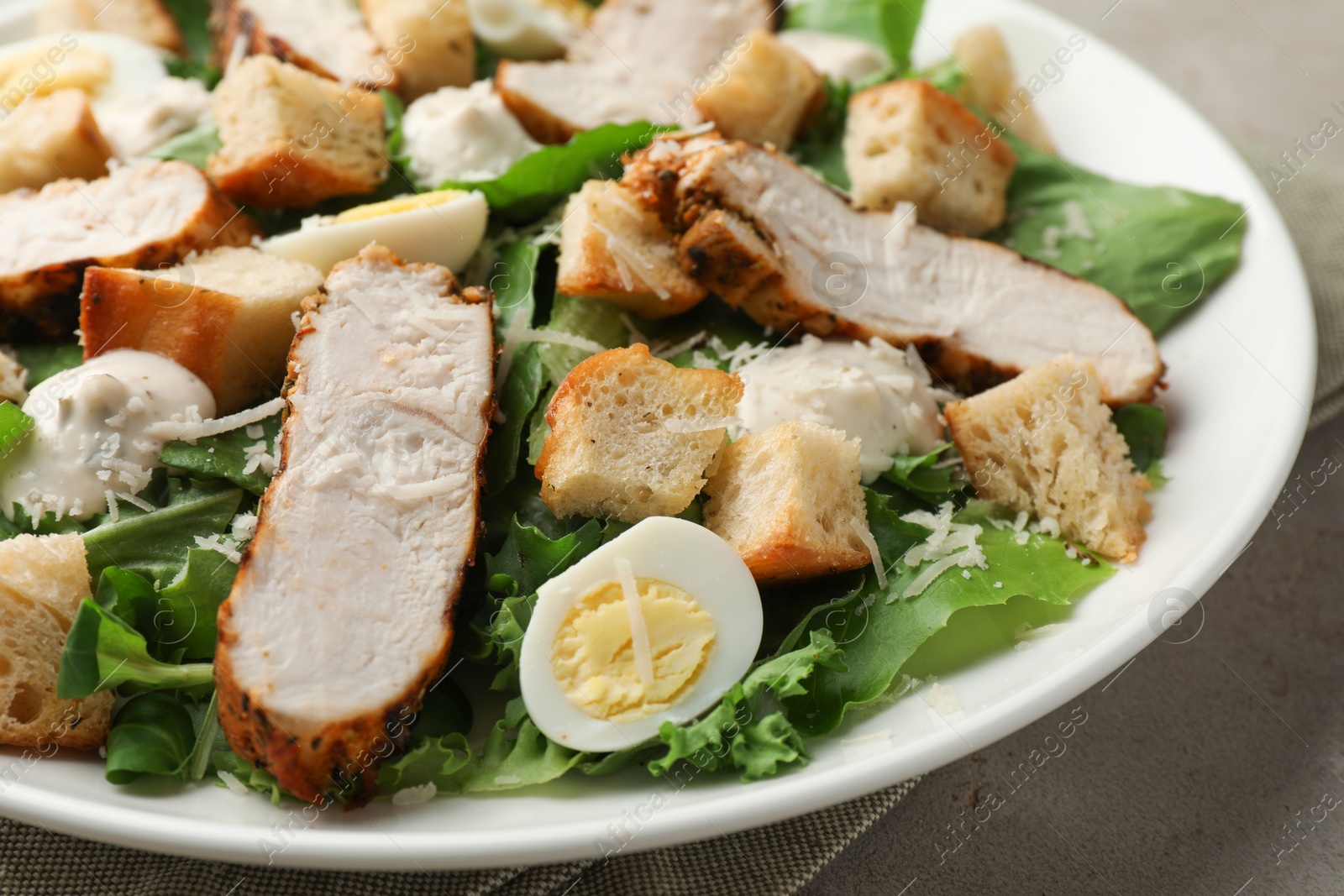 Photo of Tasty Caesar salad with chicken on light grey table, closeup