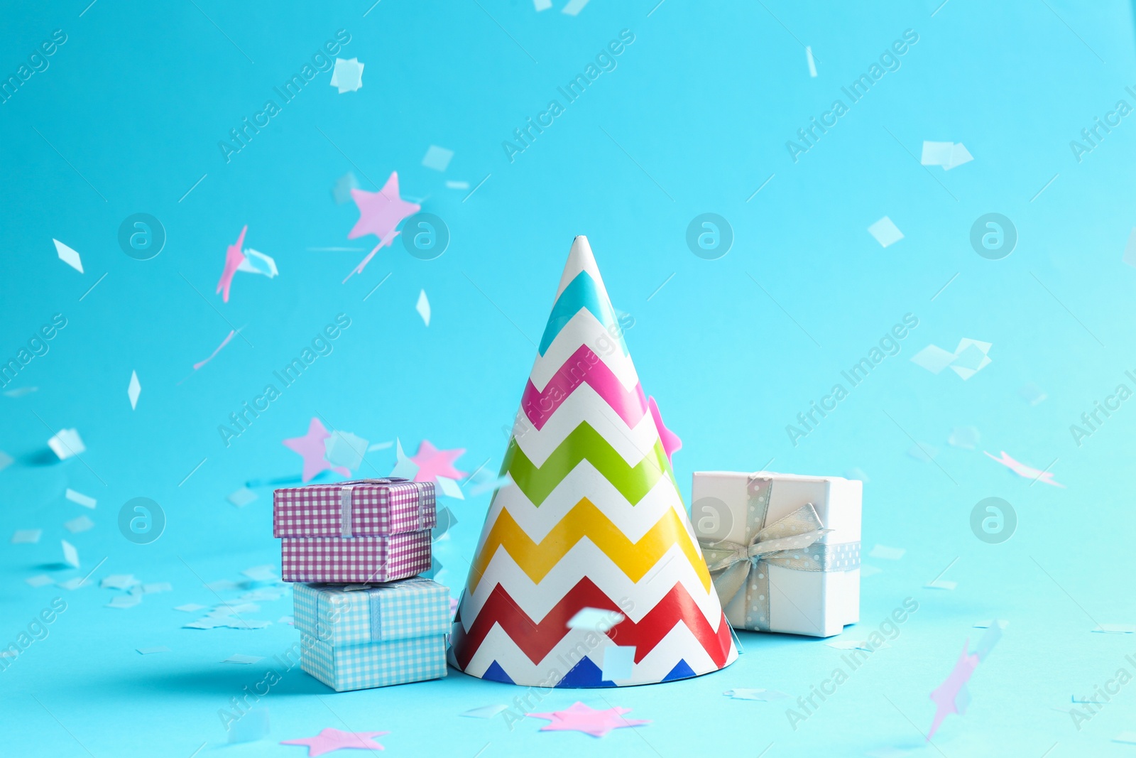 Photo of Beautiful confetti falling on party hat and gift boxes against light blue background