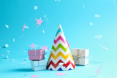 Photo of Beautiful confetti falling on party hat and gift boxes against light blue background