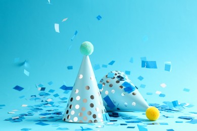 Photo of Beautiful confetti falling on party hats against light blue background