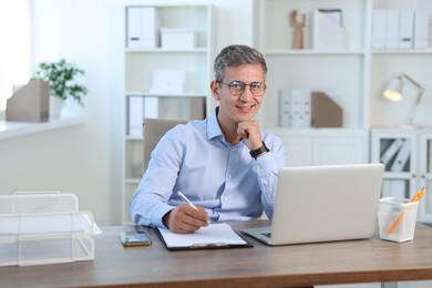 Portrait of smiling middle aged man at table in office