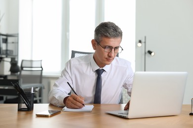 Photo of Middle aged man working with laptop at table in office