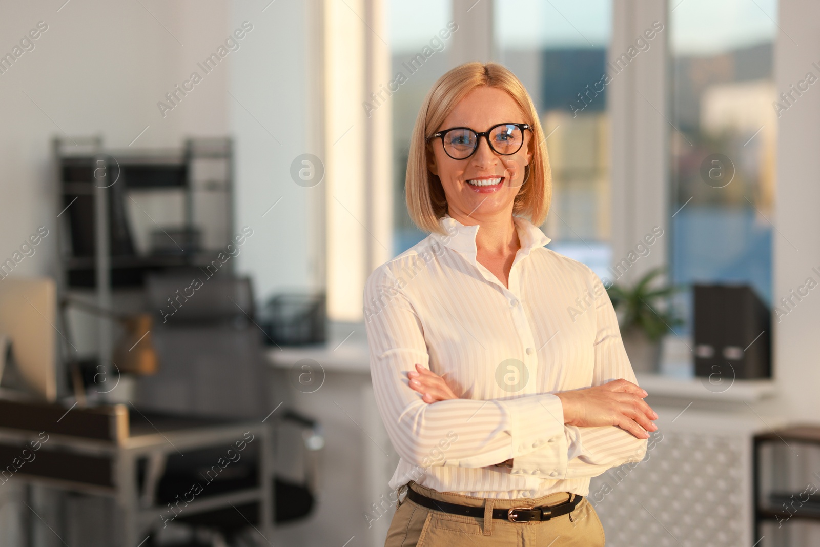 Photo of Portrait of smiling middle aged woman with crossed arms in office. Space for text