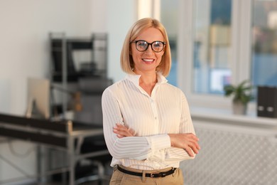 Photo of Portrait of smiling middle aged woman with crossed arms in office