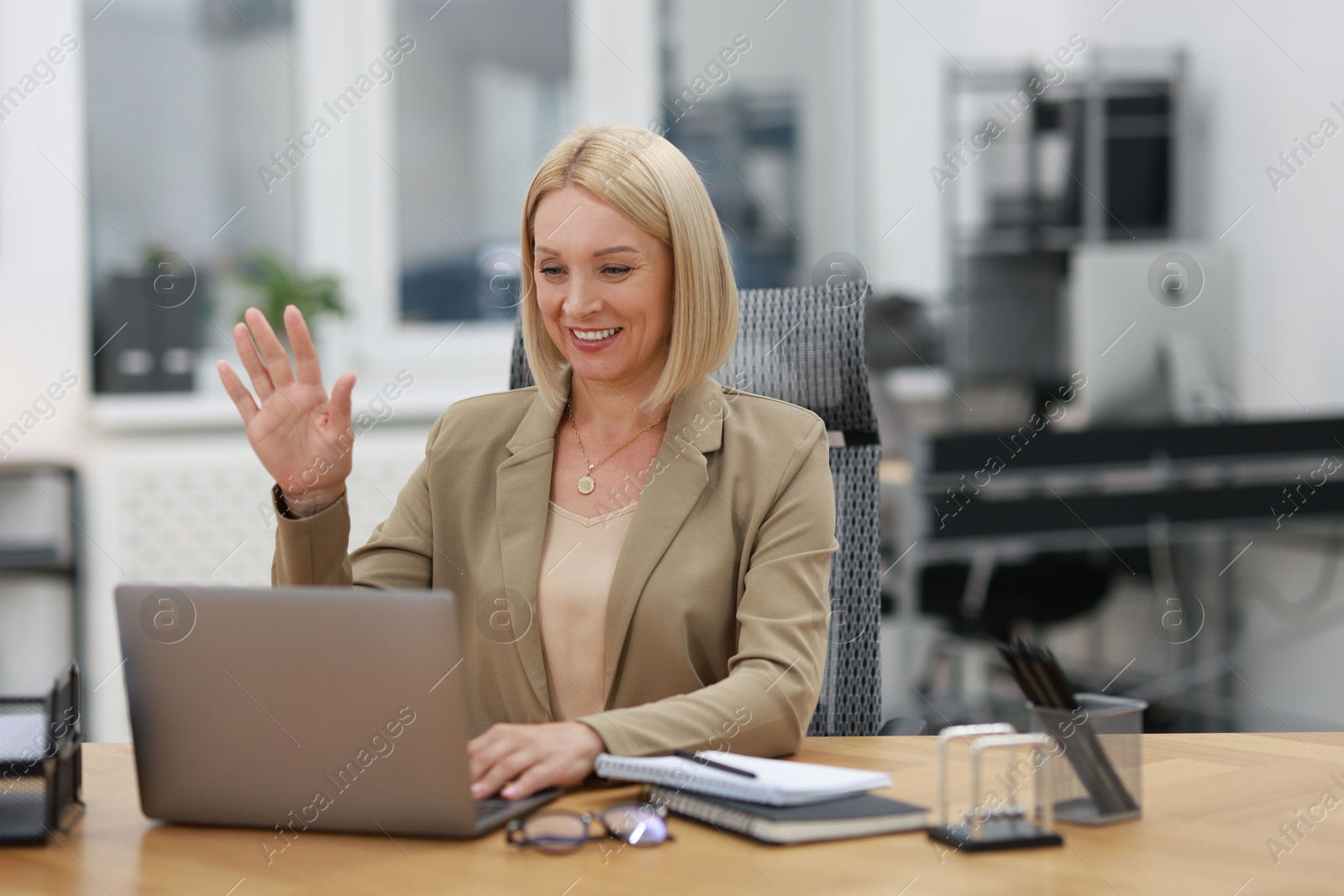 Photo of Smiling middle aged woman having videochat by laptop at table in office