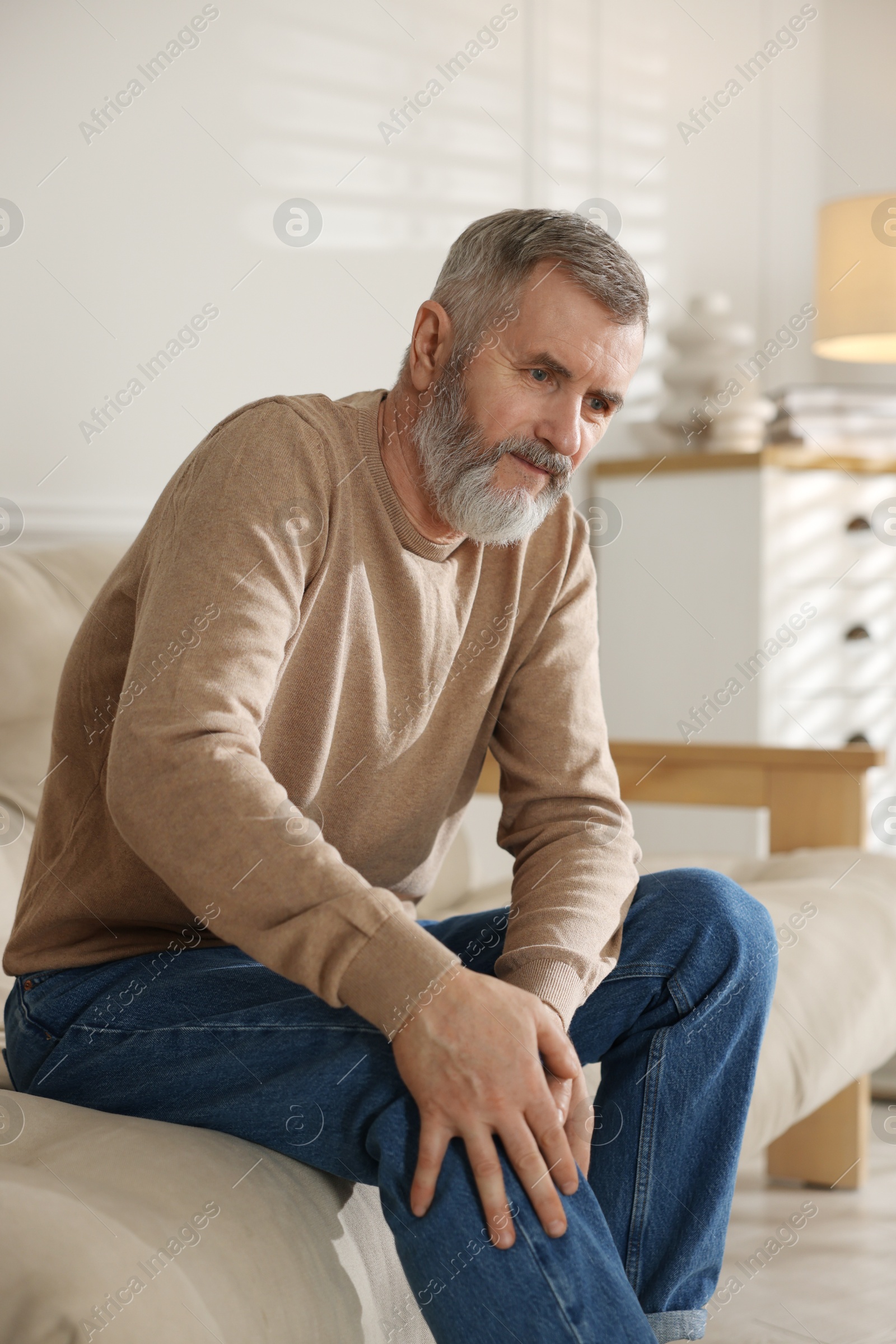 Photo of Senior man suffering from pain in knee on sofa at home