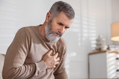 Photo of Senior man suffering from pain in chest at home, space for text