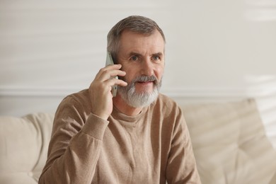 Photo of Senior man talking on smartphone at home