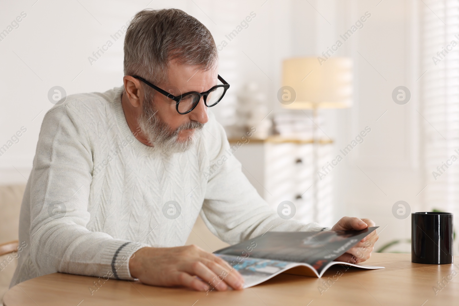 Photo of Senior man reading magazine at table indoors