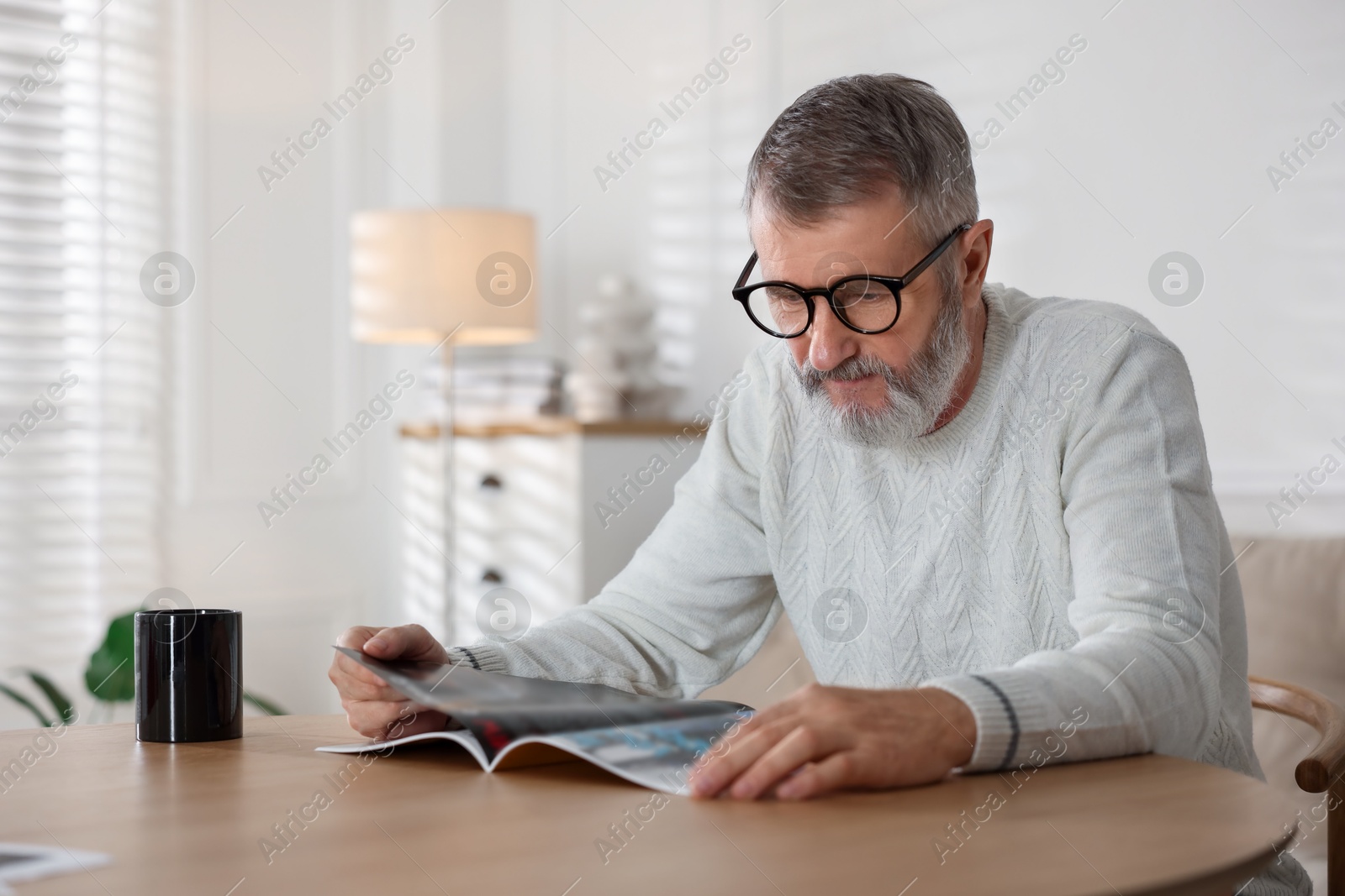 Photo of Senior man reading magazine at table indoors