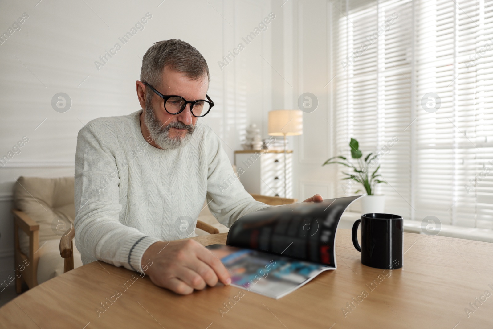 Photo of Senior man reading magazine at table indoors