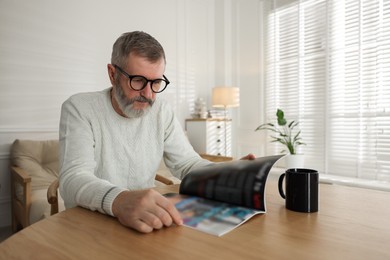 Photo of Senior man reading magazine at table indoors