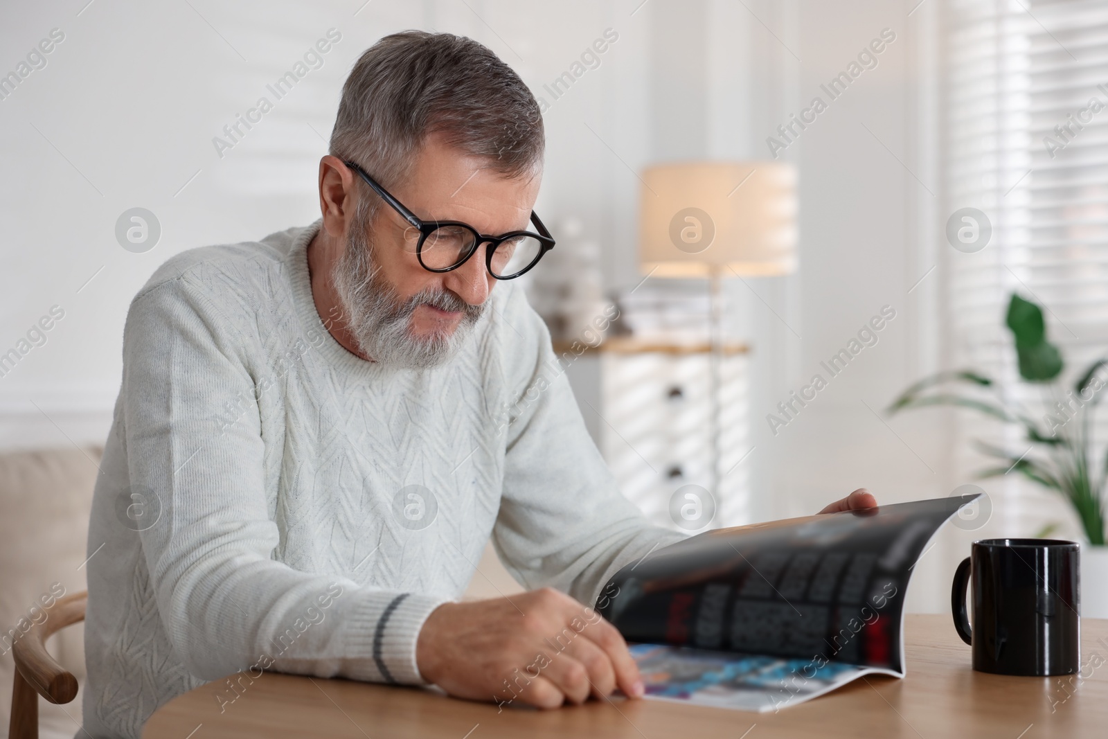 Photo of Senior man reading magazine at table indoors