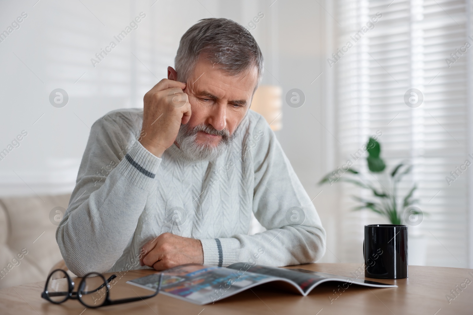 Photo of Senior man reading magazine at table indoors