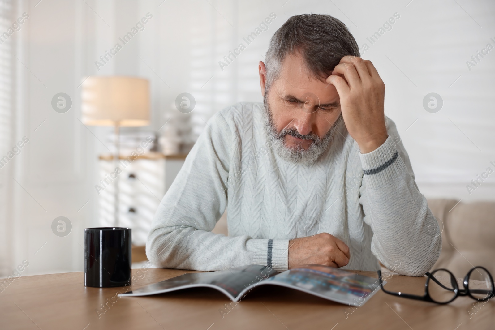 Photo of Senior man reading magazine at table indoors