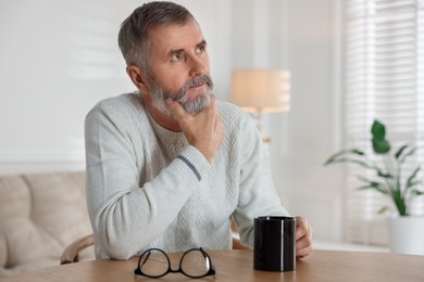 Photo of Senior man with cup of drink at table indoors