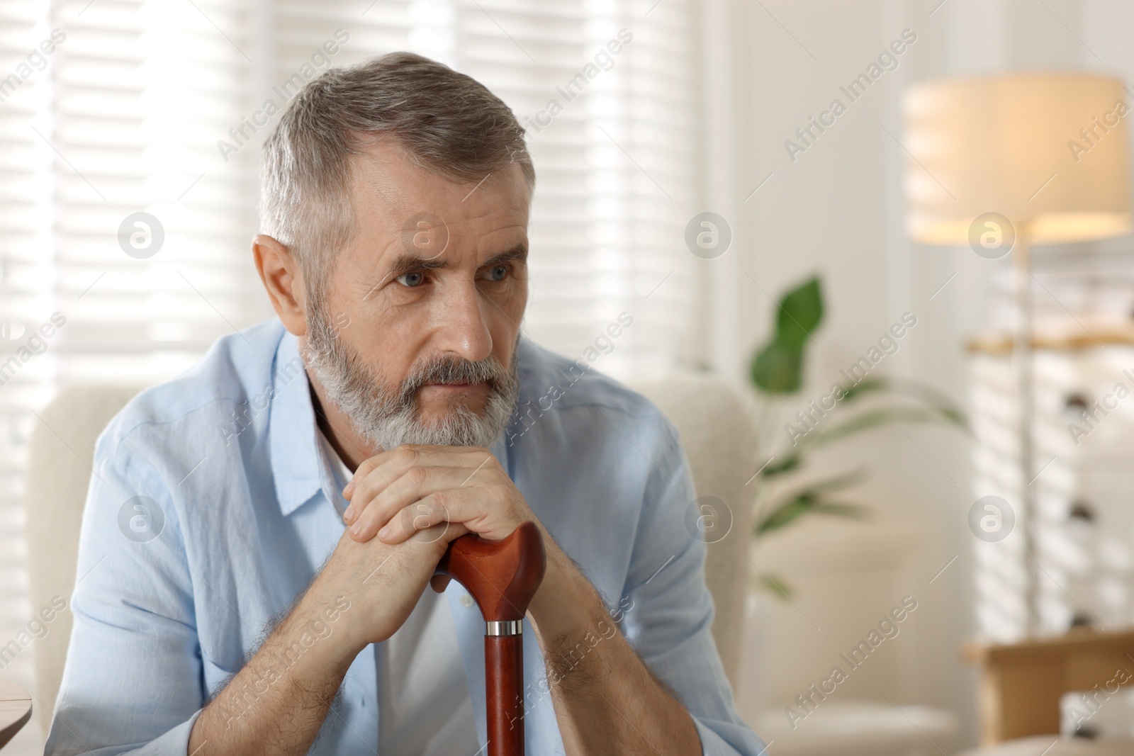 Photo of Senior man with walking cane at home, space for text