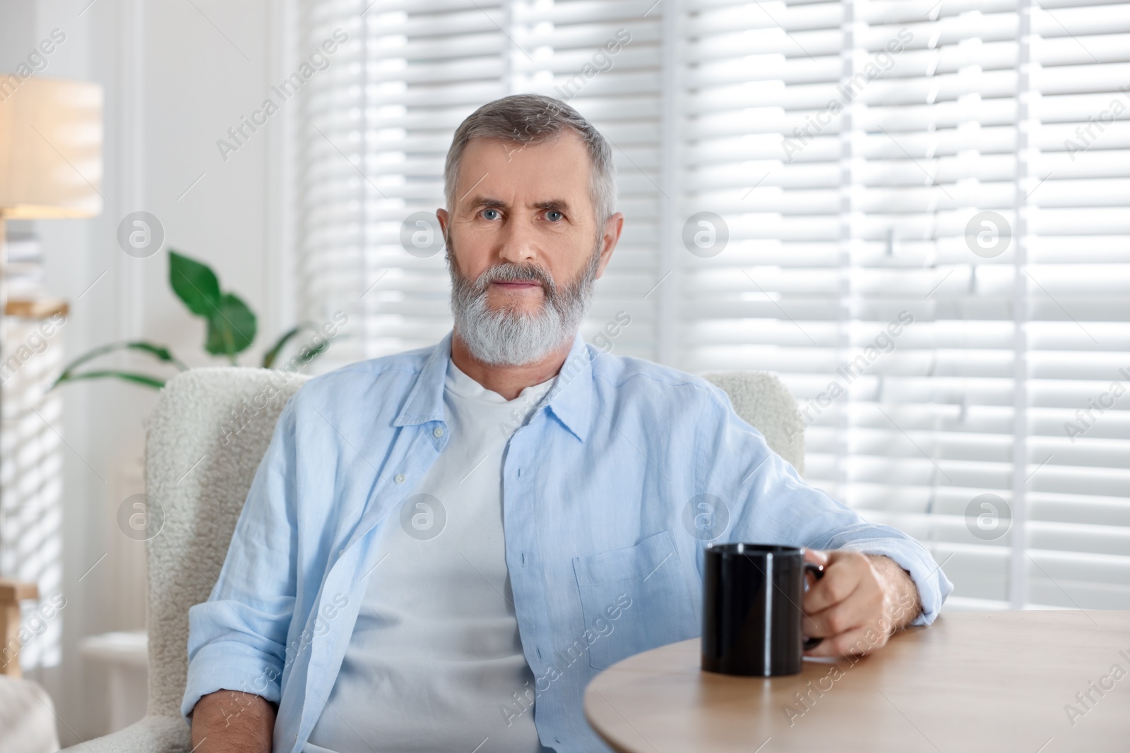 Photo of Senior man with cup of drink at table indoors