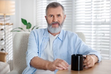 Photo of Senior man with cup of drink at table indoors