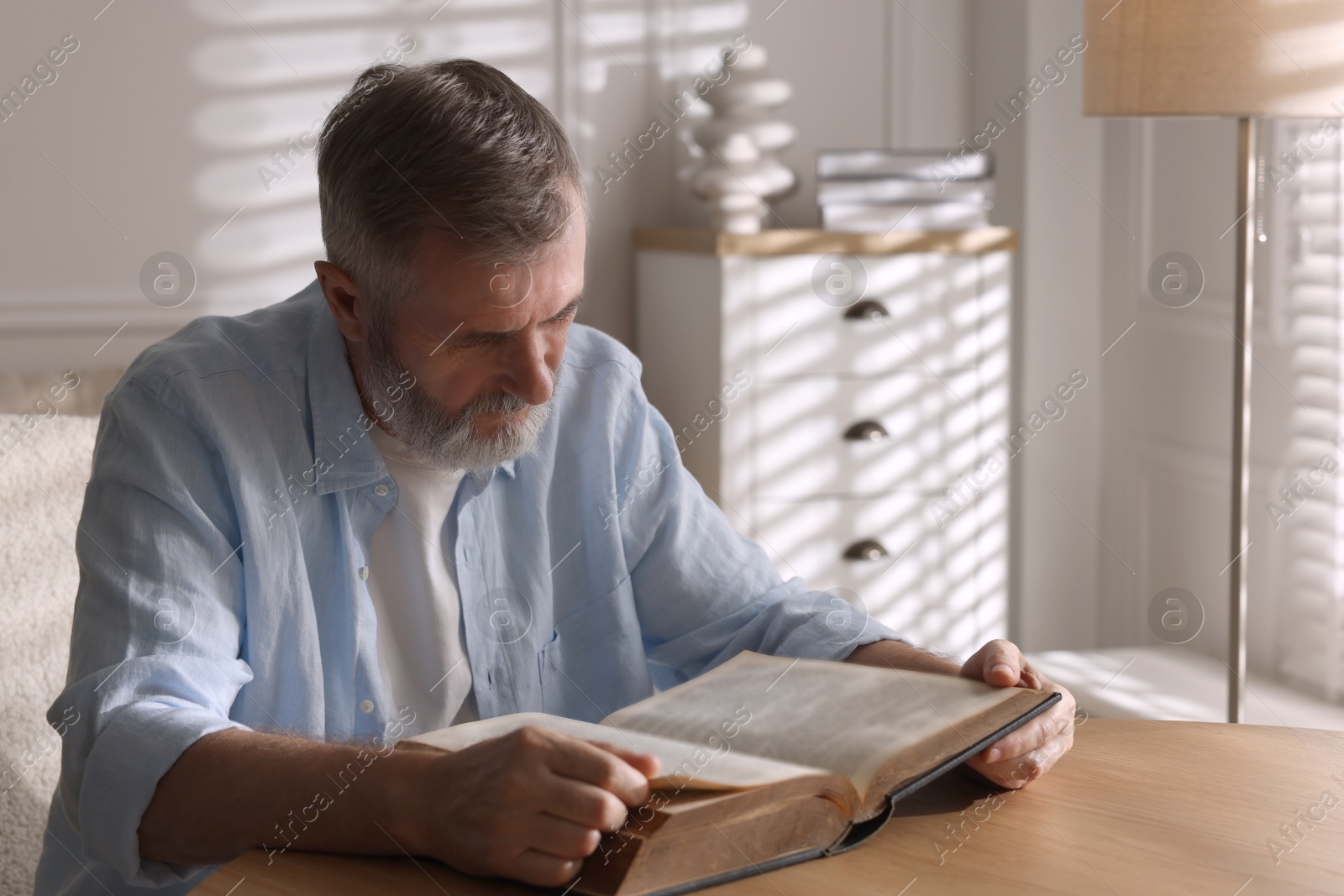 Photo of Senior man reading book at table indoors