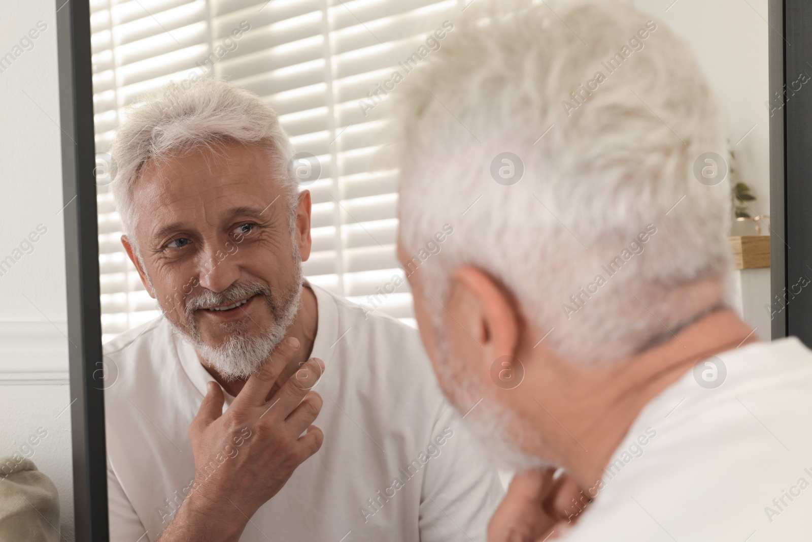 Photo of Senior man looking in mirror at home