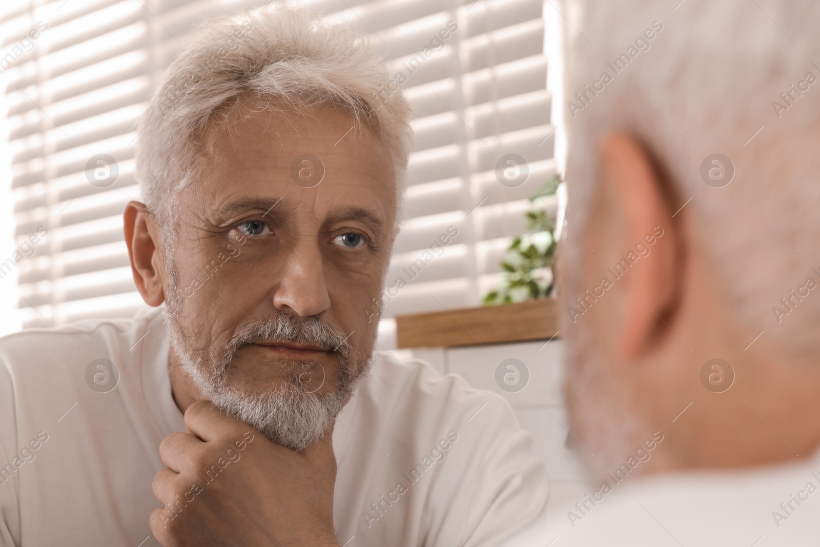 Photo of Senior man looking in mirror at home