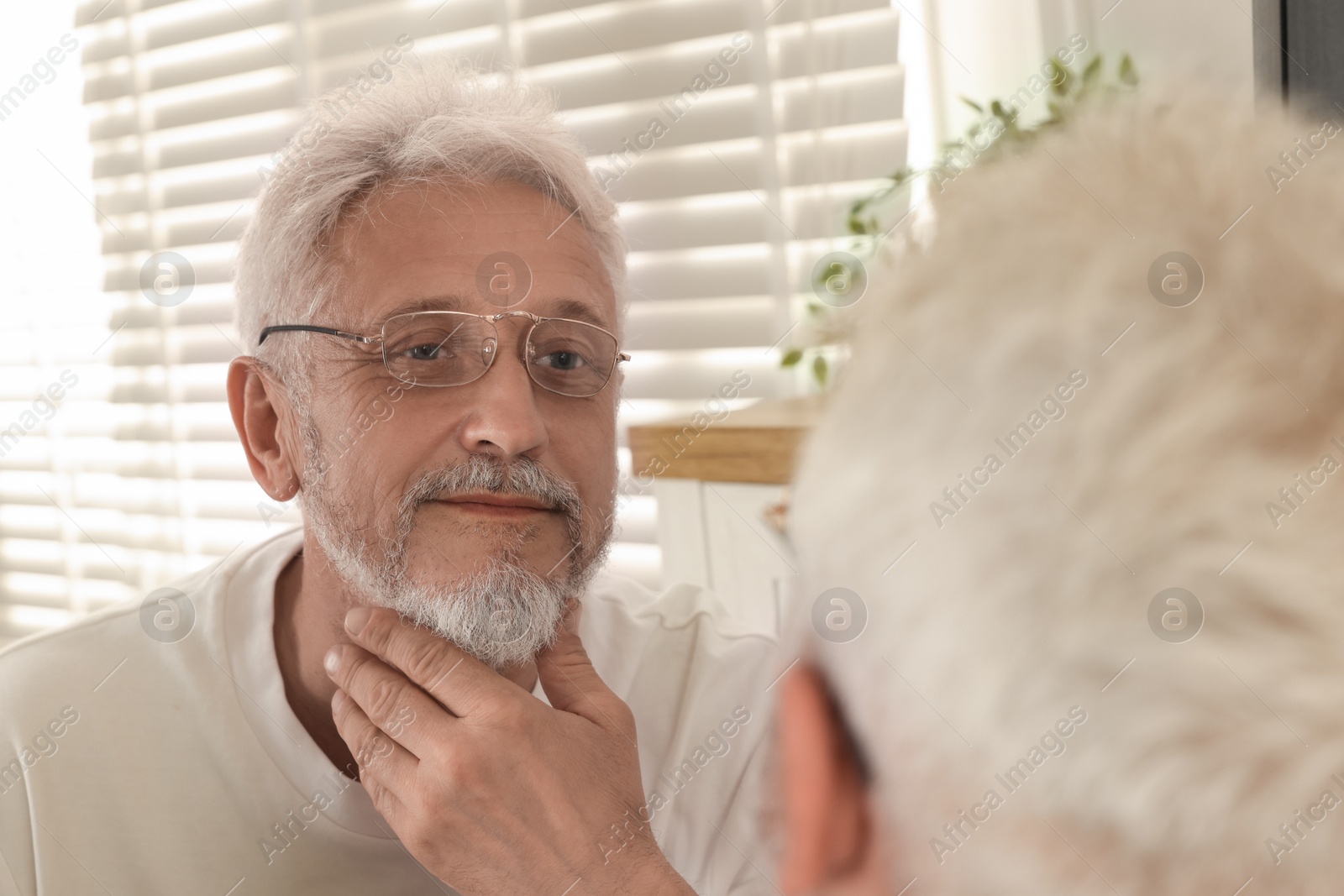 Photo of Senior man looking in mirror at home