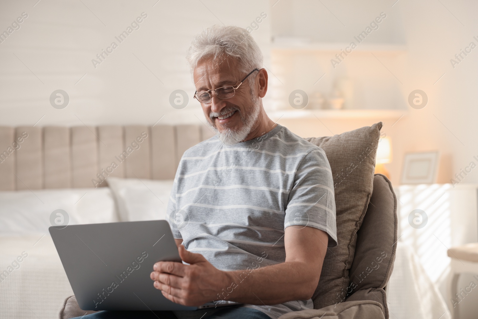 Photo of Happy senior man using laptop on armchair at home