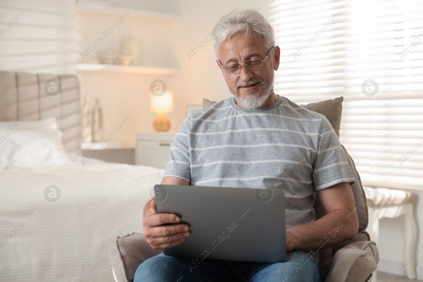 Photo of Senior man using laptop on armchair at home