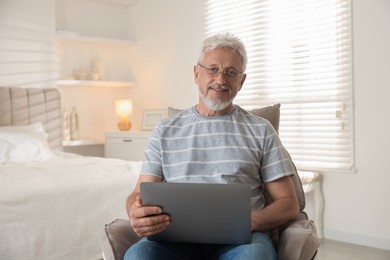 Photo of Happy senior man using laptop on armchair at home