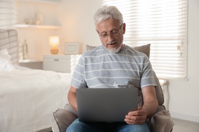 Photo of Senior man using laptop on armchair at home