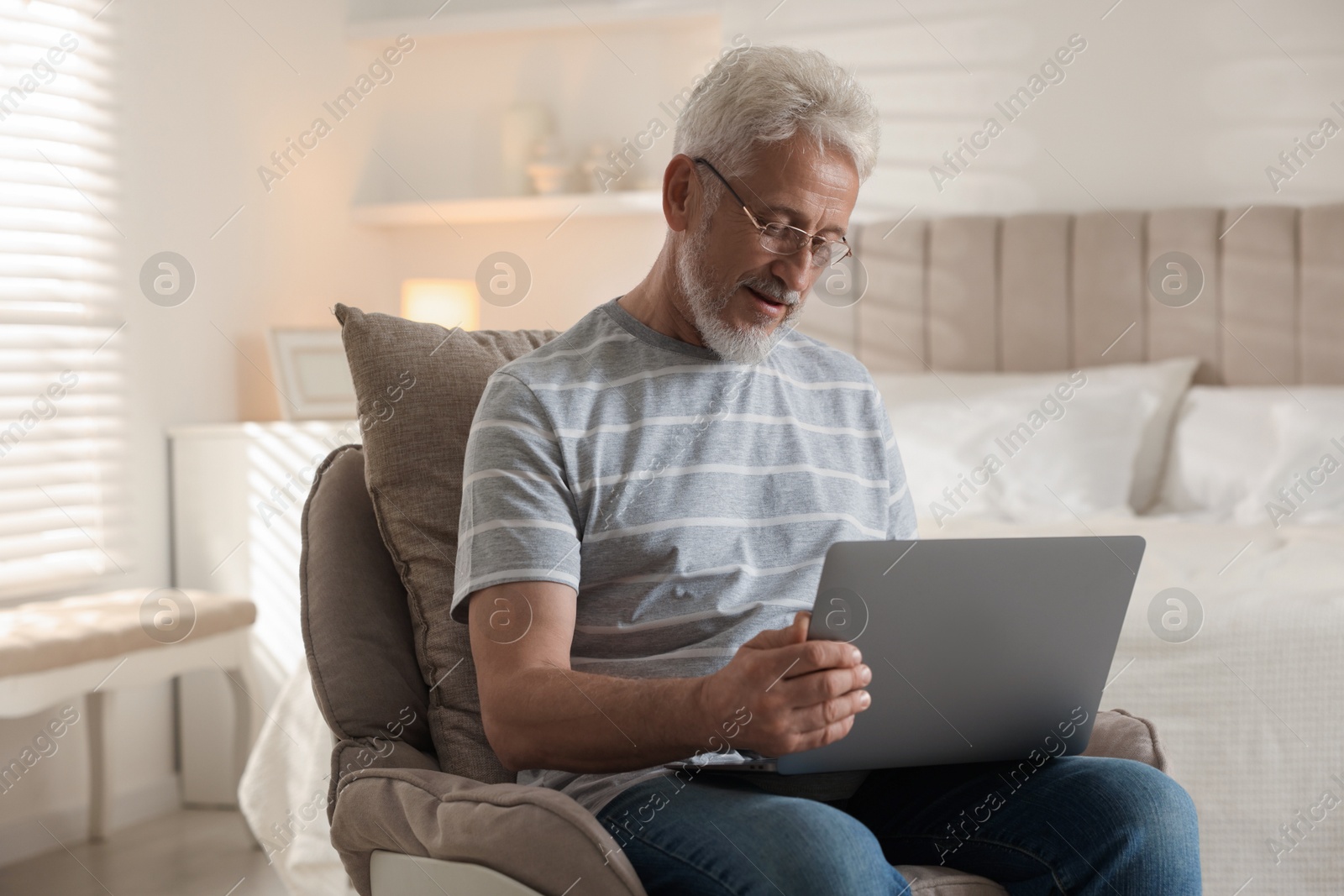 Photo of Senior man using laptop on armchair at home