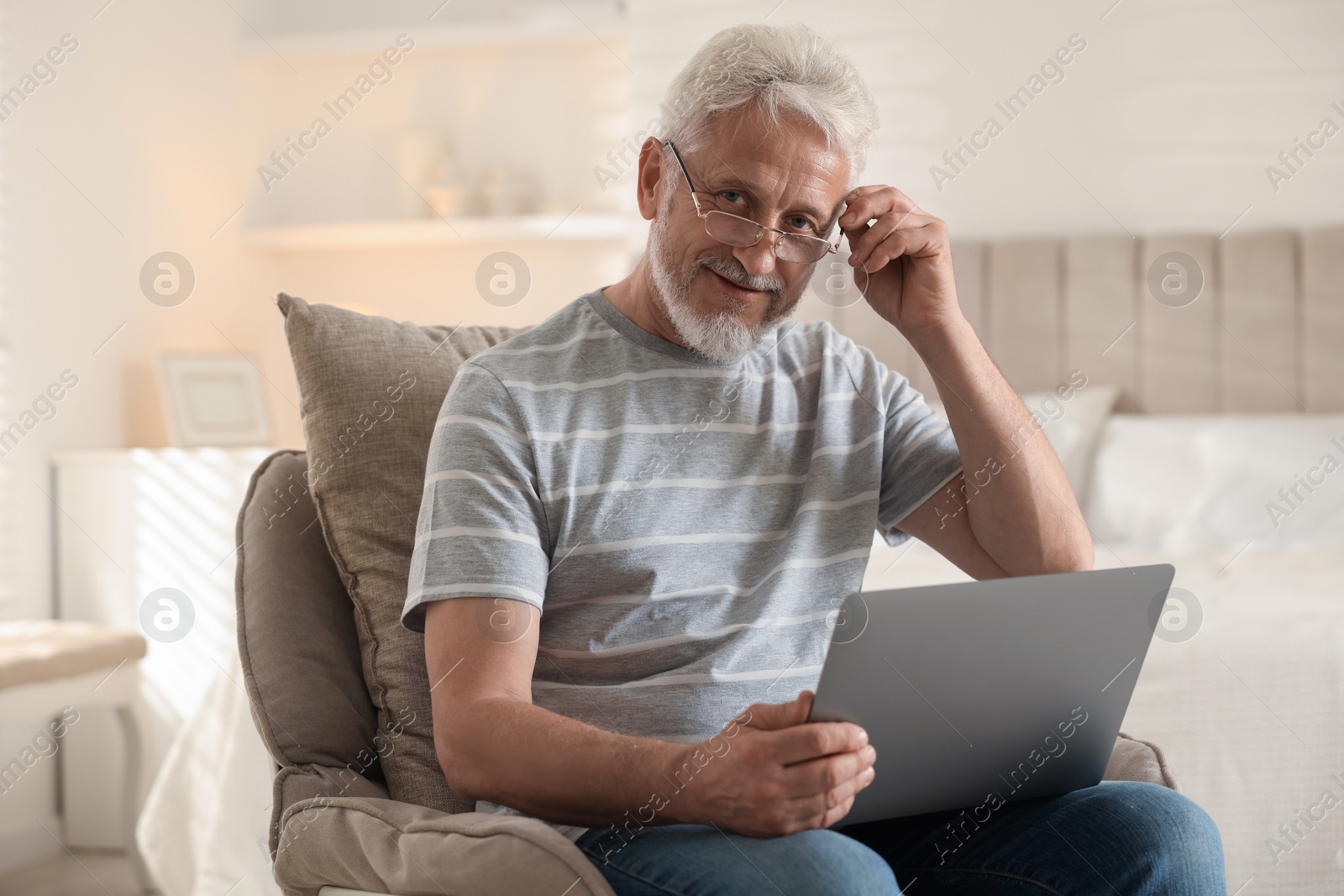 Photo of Happy senior man using laptop on armchair at home