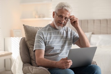 Photo of Happy senior man using laptop on armchair at home