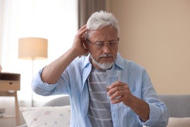 Photo of Senior man with water suffering from headache at home